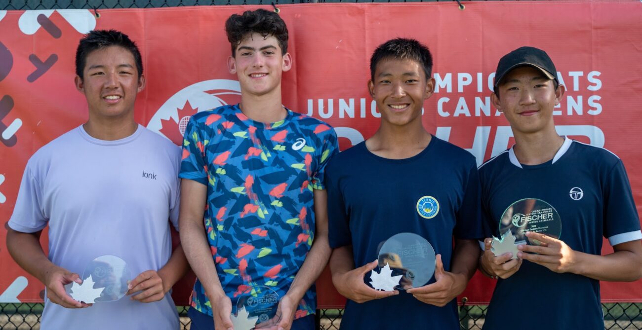 Four boys hold their trophies in front of the Fischer Junior Nationals sign.