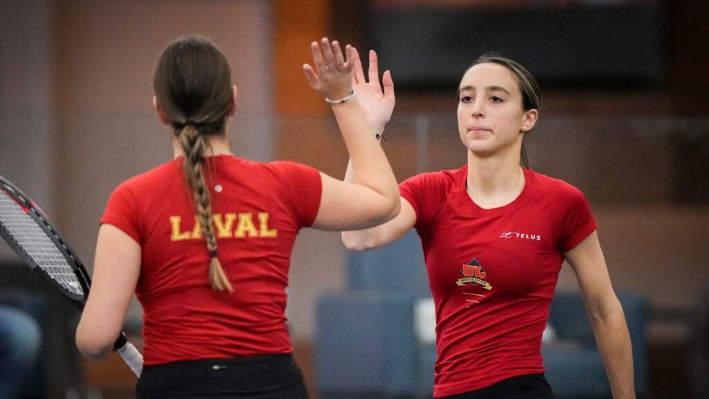 Two players for the Laval University Rouge et Or, one with back to camera and one facing, high-five.