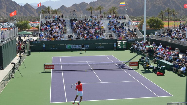 Wide shot of Gabriel Diallo (close side with back to camera) hitting a forehand in Indian Wells with the mountains in the background.